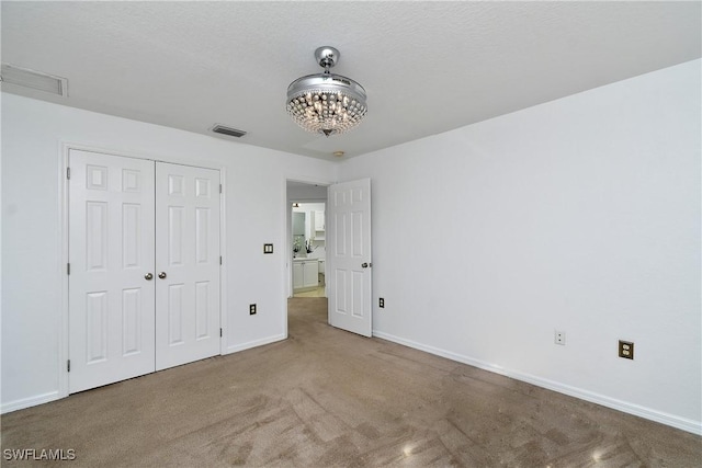 unfurnished bedroom with visible vents, baseboards, carpet floors, a closet, and a notable chandelier