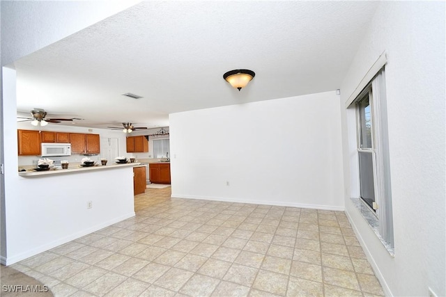 interior space with brown cabinetry, white microwave, visible vents, ceiling fan, and light countertops