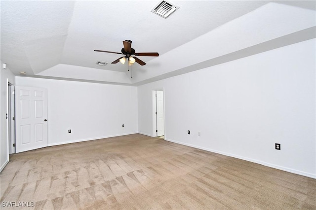 carpeted empty room with a tray ceiling, a ceiling fan, visible vents, and baseboards