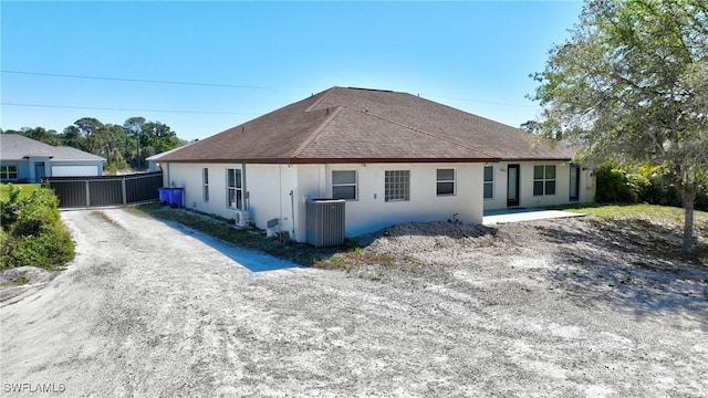 back of property featuring stucco siding, a shingled roof, central AC, and a gate