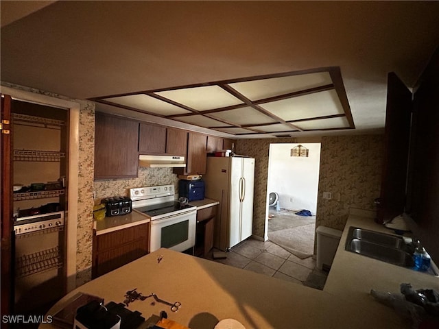 kitchen featuring dark tile patterned flooring, under cabinet range hood, a sink, white appliances, and light countertops