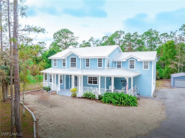 view of front of house featuring metal roof, an outbuilding, covered porch, and driveway