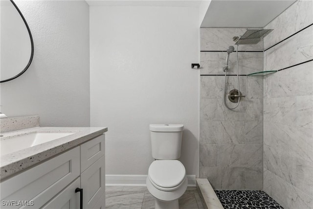 bathroom with baseboards, toilet, a tile shower, marble finish floor, and vanity