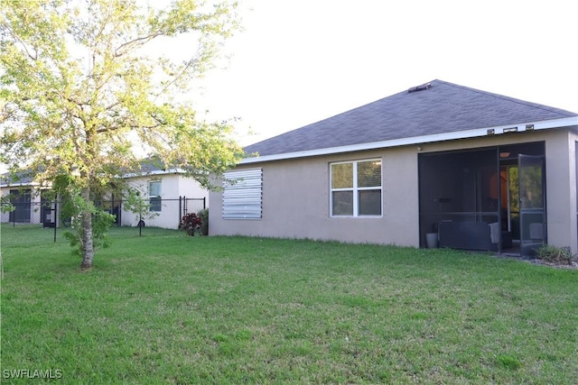 back of house with stucco siding, fence, a yard, roof with shingles, and a sunroom