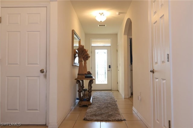 doorway with light tile patterned floors, visible vents, arched walkways, and baseboards