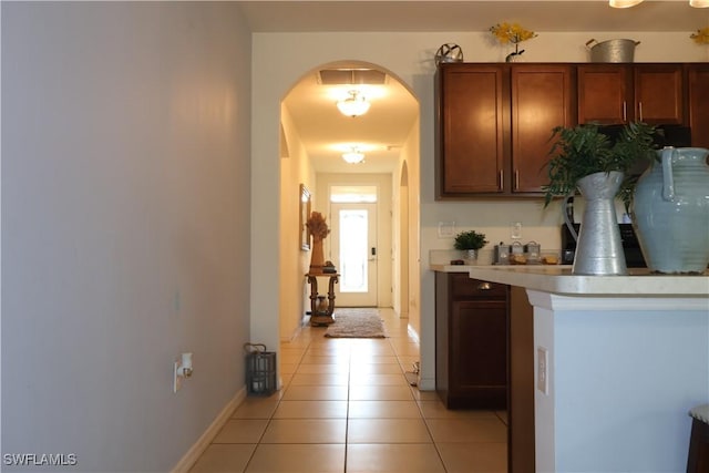 kitchen with brown cabinets, arched walkways, light countertops, light tile patterned floors, and baseboards