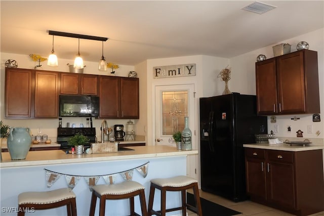 kitchen featuring visible vents, decorative light fixtures, a breakfast bar area, light countertops, and black appliances