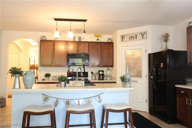 kitchen with a breakfast bar, light countertops, hanging light fixtures, black appliances, and a sink