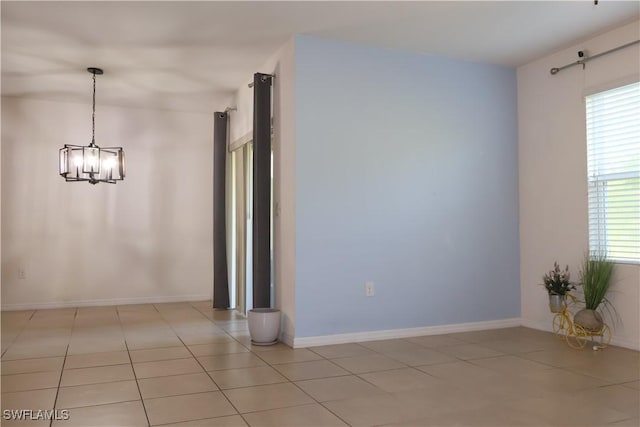 spare room with light tile patterned floors, baseboards, a wealth of natural light, and a chandelier