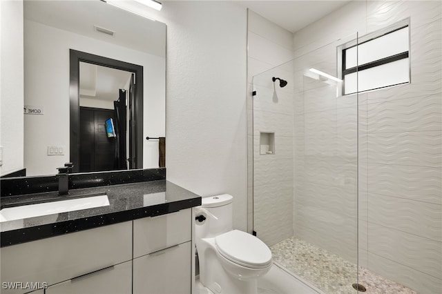 bathroom featuring a tile shower, toilet, and vanity