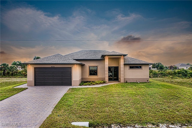 prairie-style home featuring stucco siding, a front yard, decorative driveway, and a garage