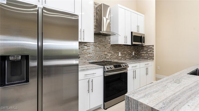 kitchen with decorative backsplash, appliances with stainless steel finishes, wall chimney exhaust hood, and white cabinets