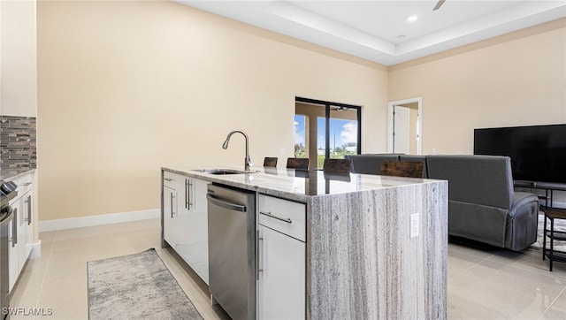 kitchen with a sink, backsplash, dishwasher, light stone counters, and a kitchen island with sink