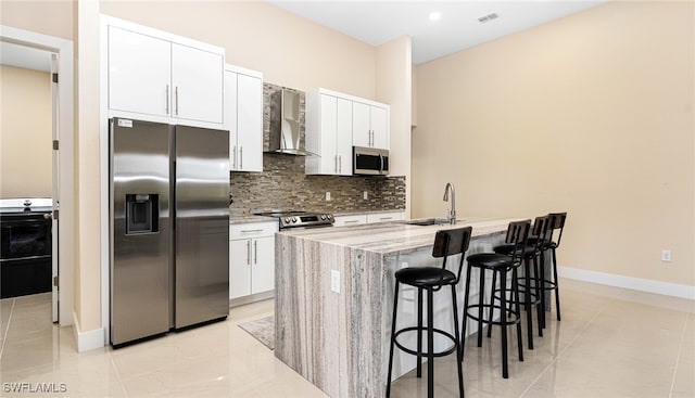 kitchen with decorative backsplash, appliances with stainless steel finishes, white cabinets, wall chimney exhaust hood, and a sink