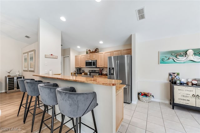 kitchen with a breakfast bar area, visible vents, a peninsula, light brown cabinetry, and appliances with stainless steel finishes