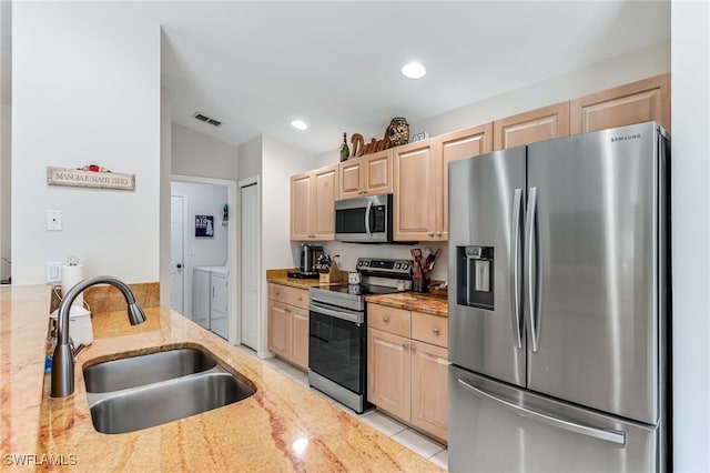 kitchen with washer and dryer, light brown cabinets, stainless steel appliances, and a sink