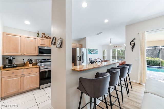 kitchen with light brown cabinets, light stone countertops, a kitchen bar, recessed lighting, and stainless steel appliances