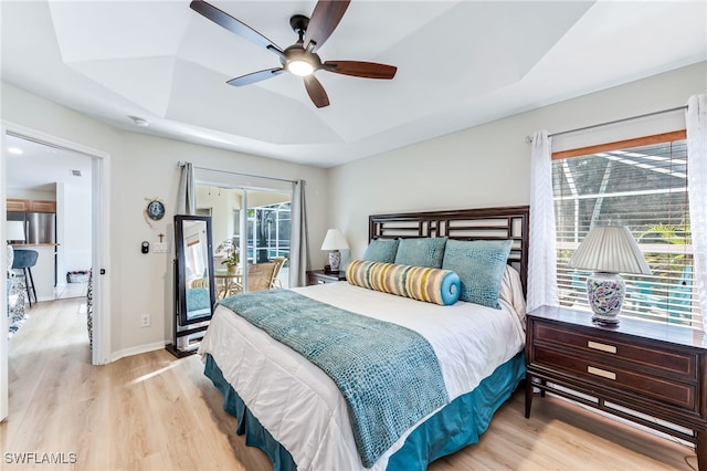 bedroom featuring baseboards, a raised ceiling, light wood-style floors, and access to exterior