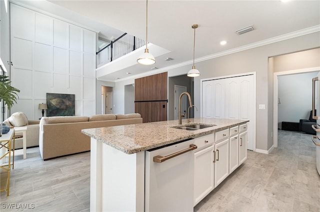 kitchen with visible vents, decorative light fixtures, an island with sink, ornamental molding, and a sink