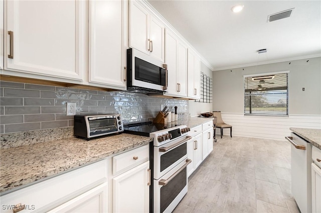 kitchen featuring visible vents, white cabinets, white appliances, and a wainscoted wall