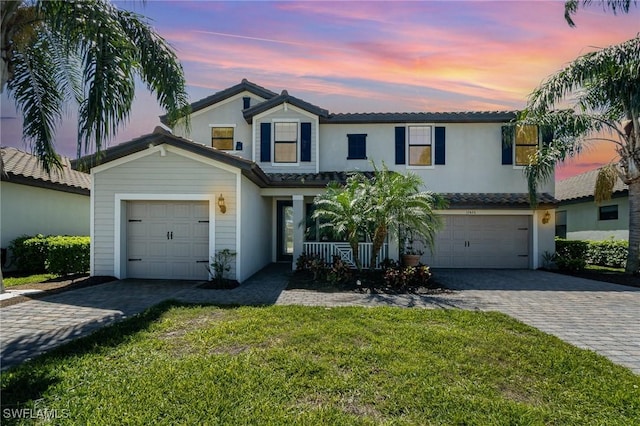 view of front of house with a tiled roof, decorative driveway, a lawn, and stucco siding