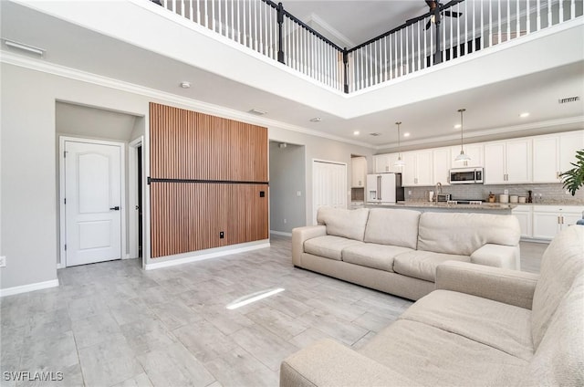 living area featuring visible vents, a high ceiling, crown molding, and baseboards
