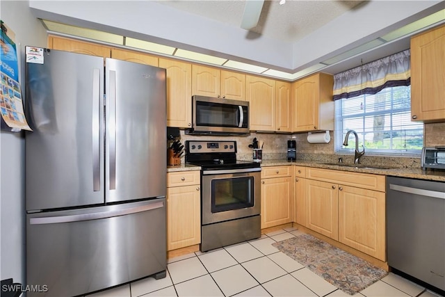 kitchen featuring a sink, light stone countertops, appliances with stainless steel finishes, and light brown cabinetry