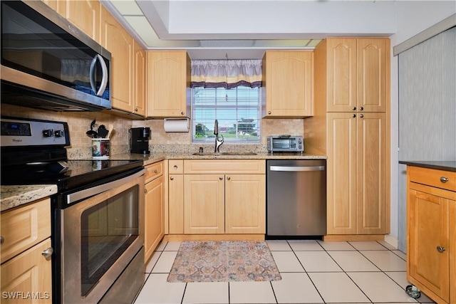 kitchen with light stone counters, light brown cabinets, a sink, appliances with stainless steel finishes, and tasteful backsplash