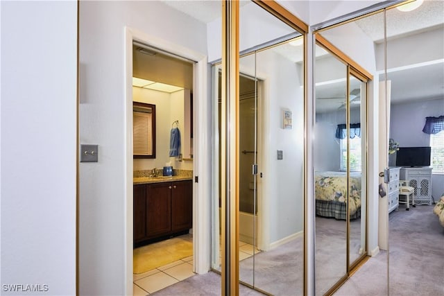 hallway with light tile patterned floors, light colored carpet, and a sink