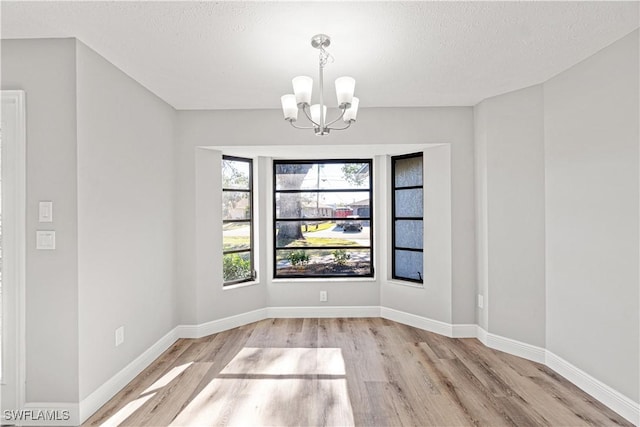 unfurnished dining area with a notable chandelier, wood finished floors, baseboards, and a textured ceiling