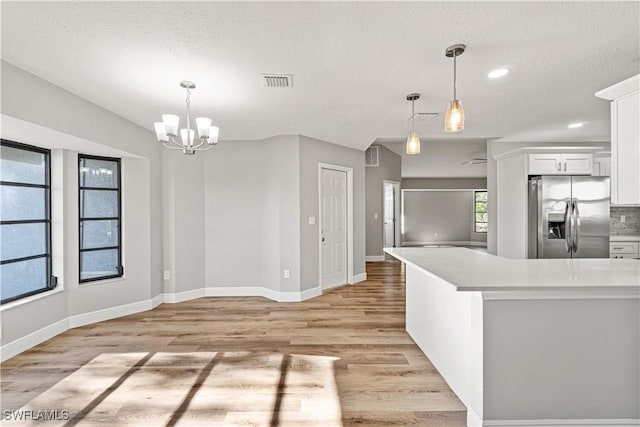 kitchen with visible vents, light countertops, white cabinets, light wood-style floors, and stainless steel fridge