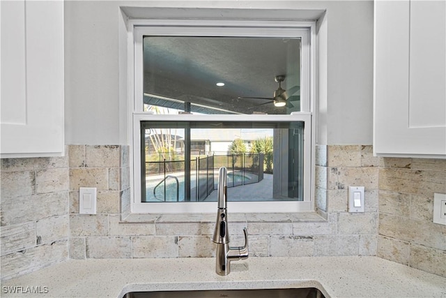 room details featuring ceiling fan, white cabinets, light stone countertops, and a sink