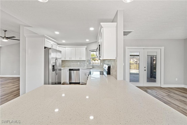 kitchen with backsplash, light stone countertops, french doors, stainless steel appliances, and white cabinetry