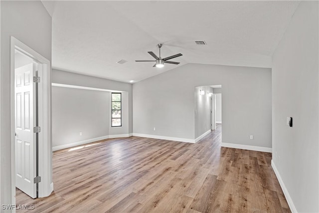 empty room featuring a ceiling fan, visible vents, baseboards, light wood-style flooring, and vaulted ceiling