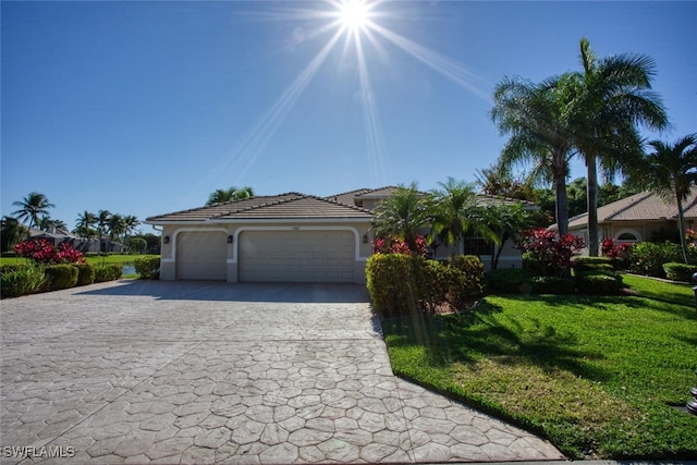 view of front facade with a front yard, an attached garage, stucco siding, a tile roof, and decorative driveway