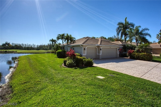 view of home's exterior featuring an attached garage, a yard, a water view, a tile roof, and decorative driveway