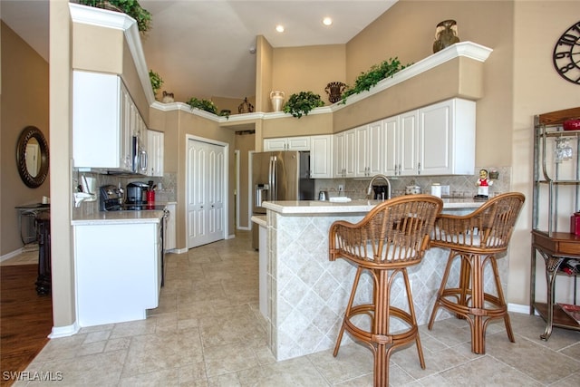 kitchen with light countertops, a peninsula, a high ceiling, white cabinets, and a sink