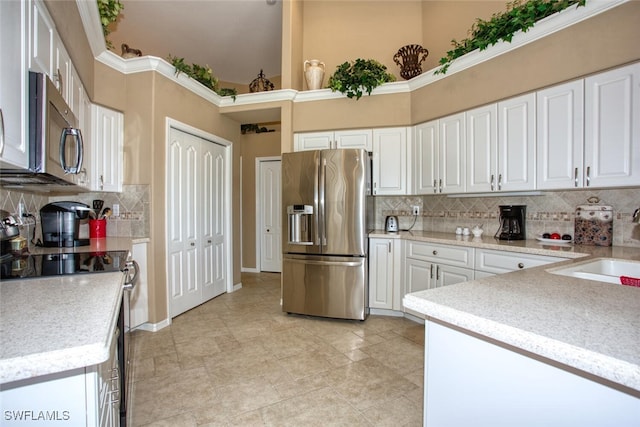 kitchen with a sink, white cabinetry, stainless steel appliances, decorative backsplash, and baseboards