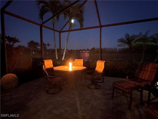 patio at night featuring glass enclosure and an outdoor fire pit