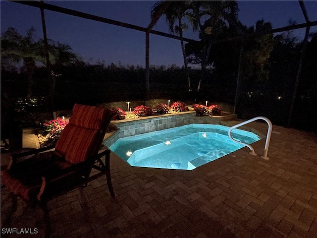 pool at night featuring glass enclosure, a patio, and an in ground hot tub