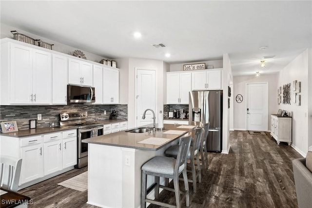 kitchen with visible vents, a breakfast bar, a kitchen island with sink, a sink, and appliances with stainless steel finishes