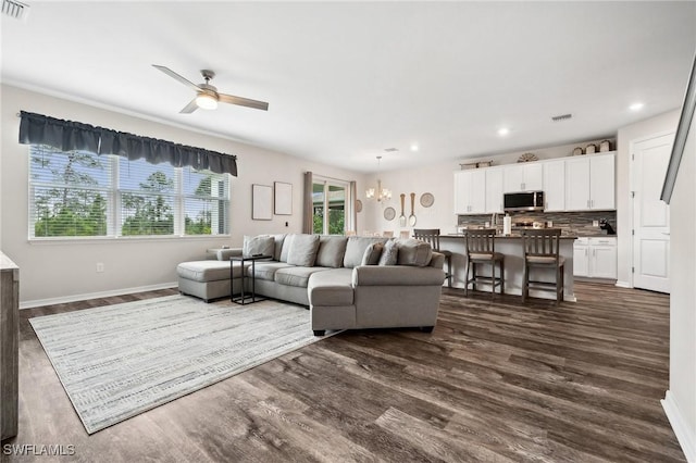 living area featuring visible vents, ceiling fan with notable chandelier, dark wood-type flooring, and baseboards