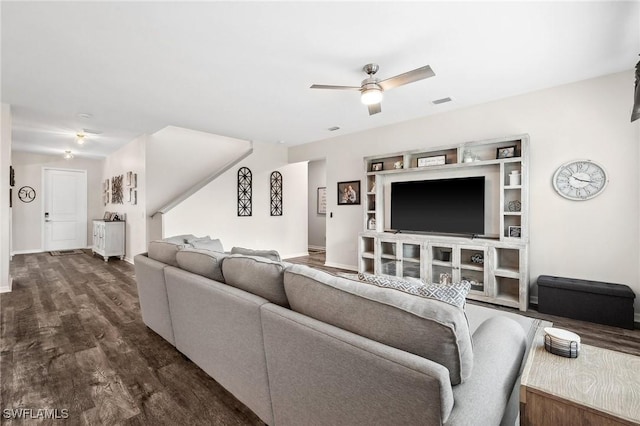 living room featuring ceiling fan, visible vents, baseboards, and dark wood-style floors