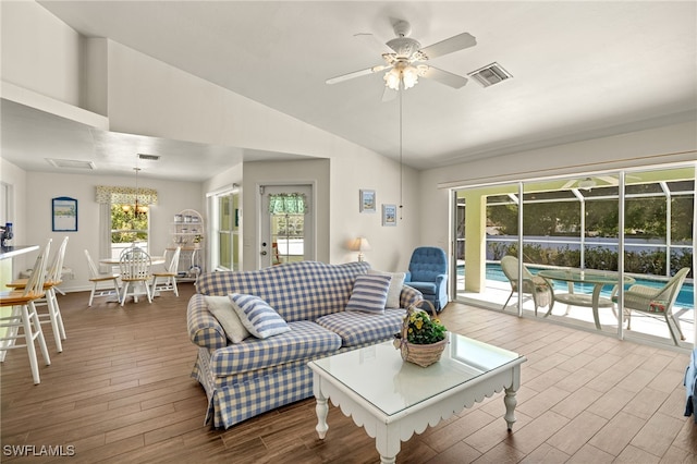 living area featuring visible vents, lofted ceiling, wood finished floors, and ceiling fan with notable chandelier