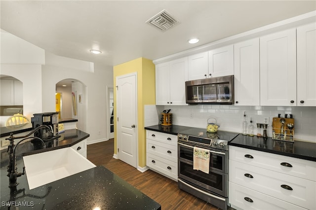 kitchen featuring visible vents, a sink, dark wood finished floors, stainless steel appliances, and arched walkways