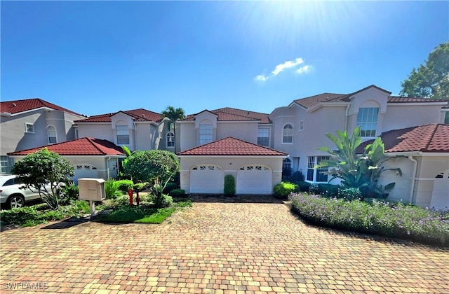 mediterranean / spanish-style house featuring stucco siding, a tile roof, decorative driveway, a residential view, and an attached garage