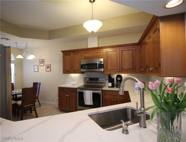 kitchen featuring brown cabinetry, pendant lighting, baseboards, a sink, and appliances with stainless steel finishes