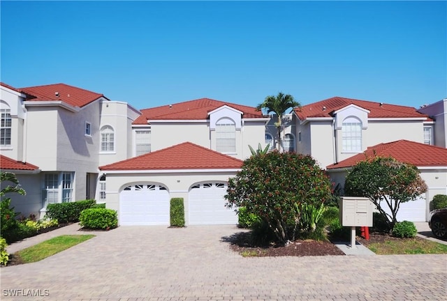 mediterranean / spanish home featuring stucco siding, decorative driveway, a tile roof, and a garage