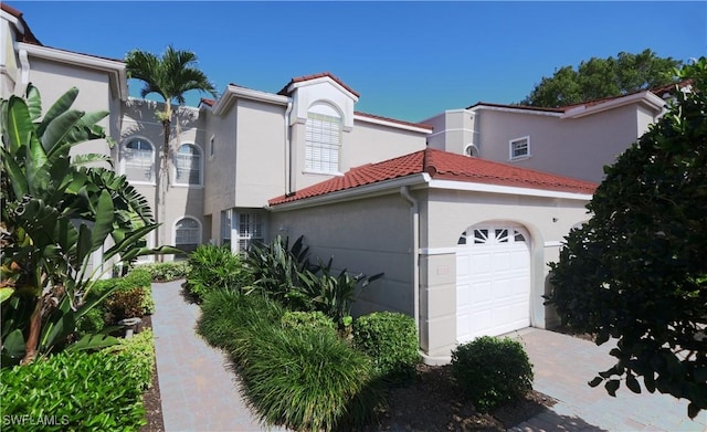 mediterranean / spanish-style house with stucco siding, a tiled roof, and an attached garage