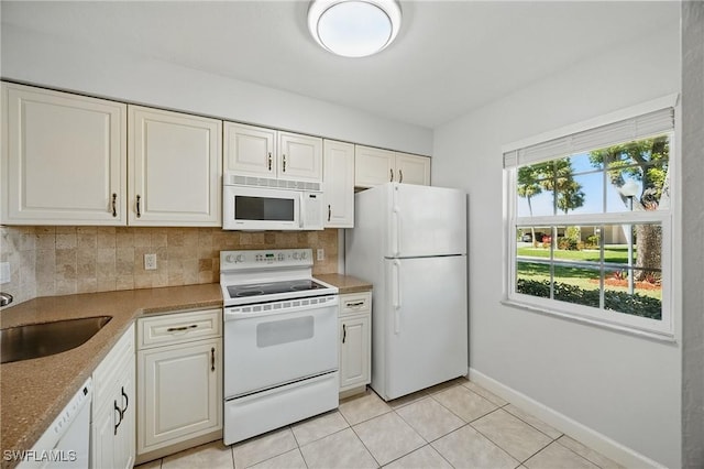 kitchen featuring white appliances, light tile patterned floors, a sink, white cabinets, and backsplash